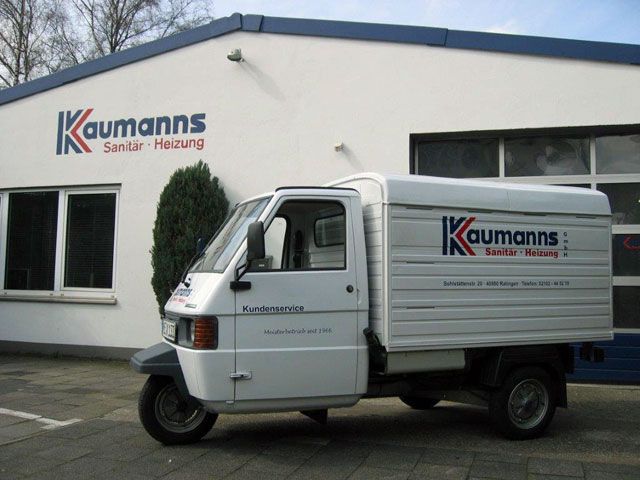 Dreirädriges Kundendienstfahrzeug mit „Kaufmanns Sanitär • Heizung“-Logo steht vor dem gleichnamigen Firmengebäude.